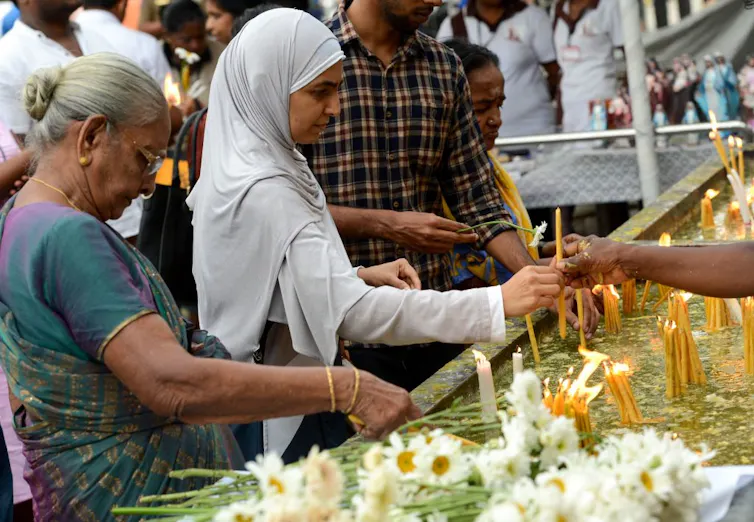 Rising up right through Sri Lanka’s civil battle taught me that obtaining in conjunction with other people throughout divides is a distinctive feature we will be informed 4 A woman with gray hair, wearing a blue-green outfit, and a younger woman in a white head covering light candles at a stall outside.