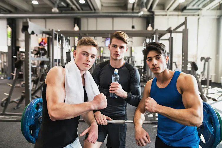 Trois jeunes hommes exhibant leurs muscles dans une salle de sport