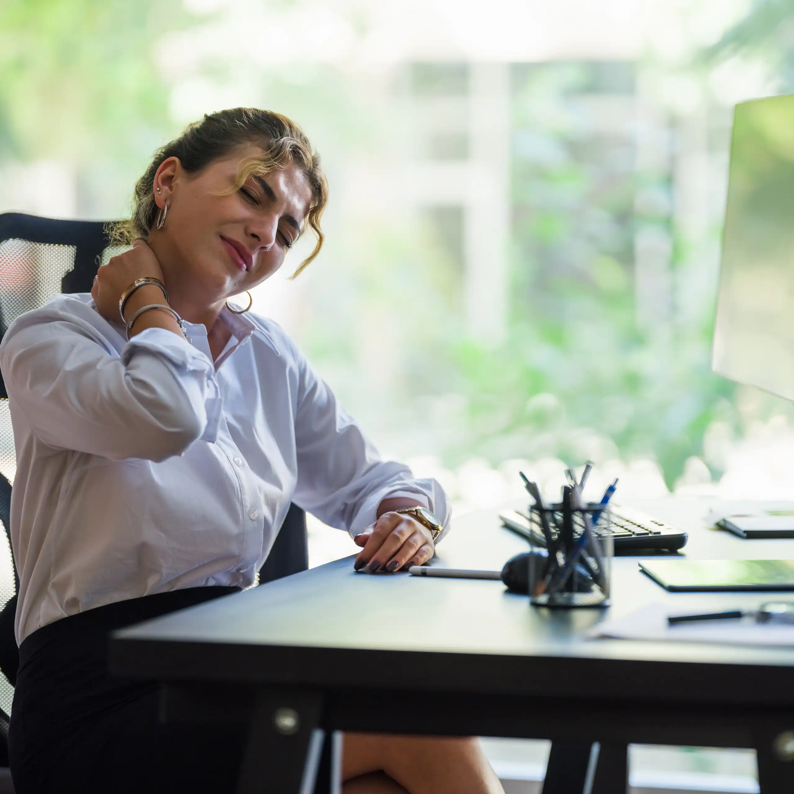 Businesswoman whose neck is hurting sits at a desk at work.