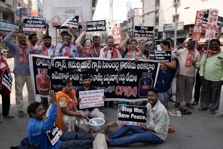 Protesters carrying a sign on a street, with some of them sitting down and others standing.