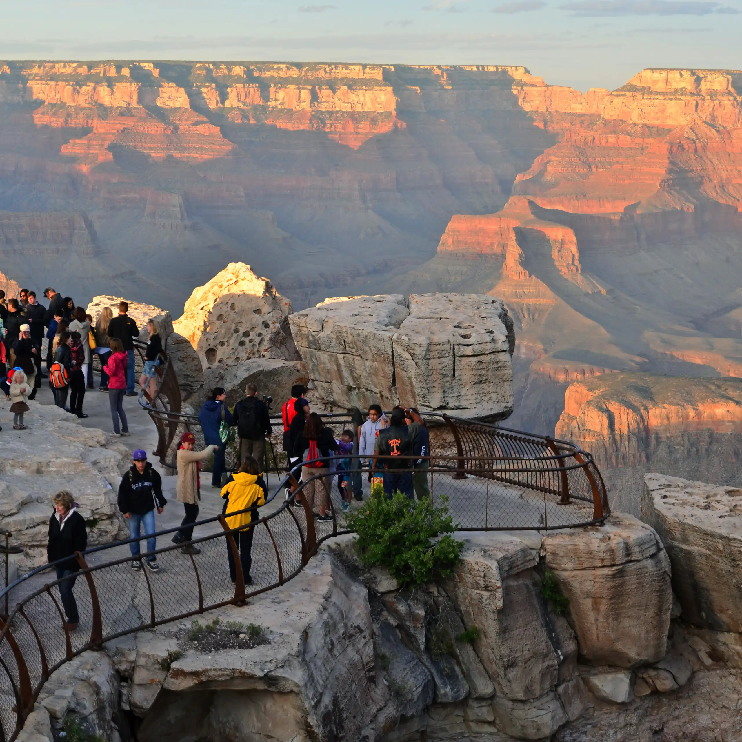 A view of a massive canyon landscape with a condensed group of people on a platform overlooking the space.