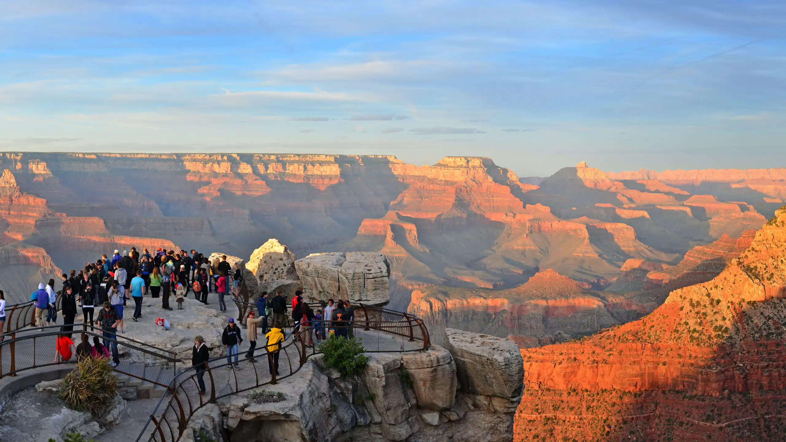 A view of a massive canyon landscape with a condensed group of people on a platform overlooking the space.