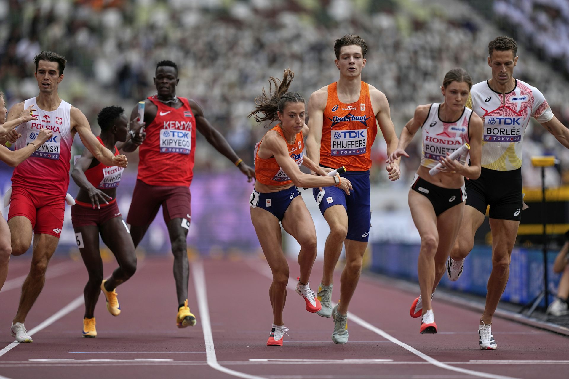 Men and women sprinters handing off batons during a relay race