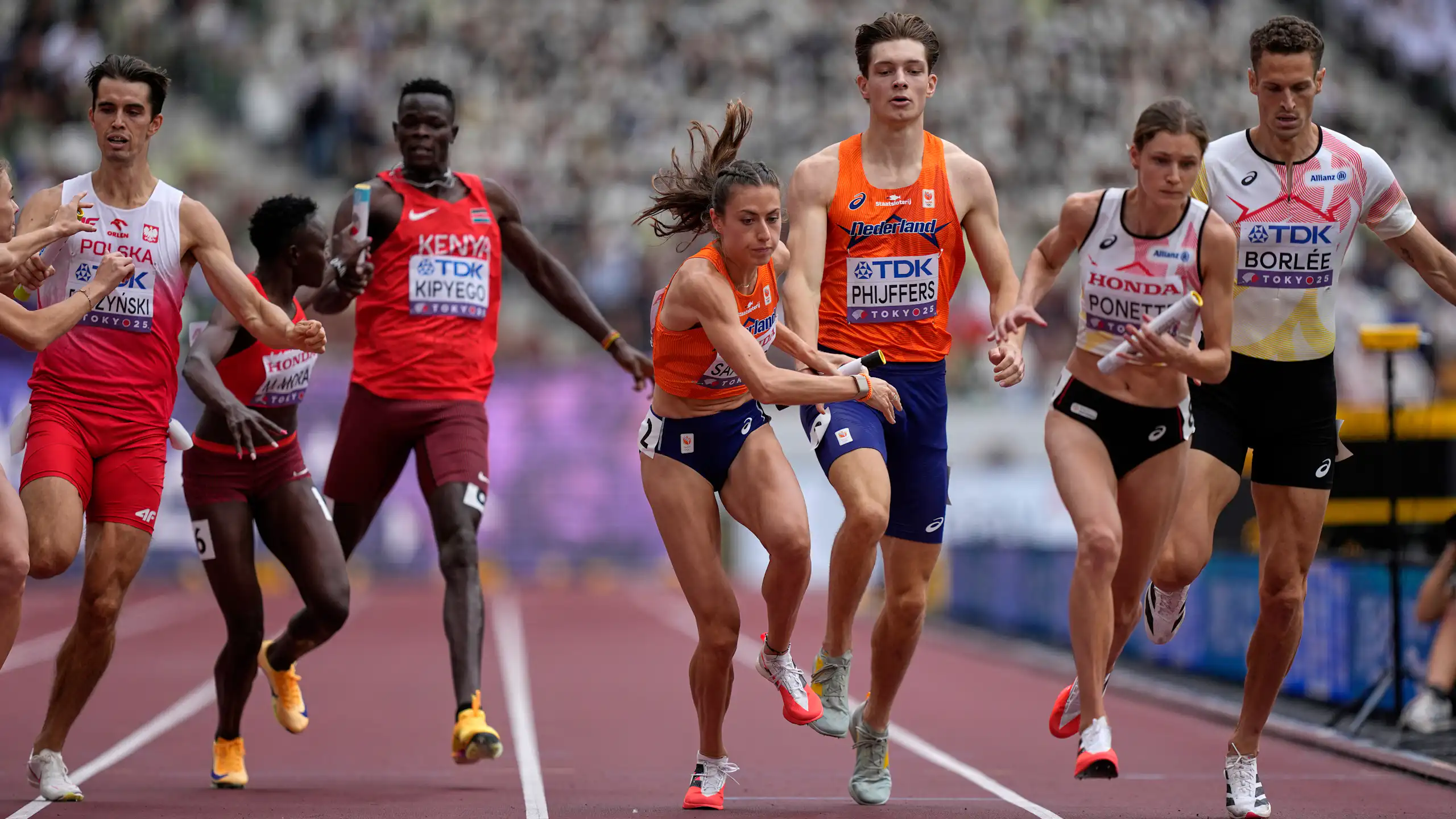 Men and women sprinters handing off batons during a relay race
