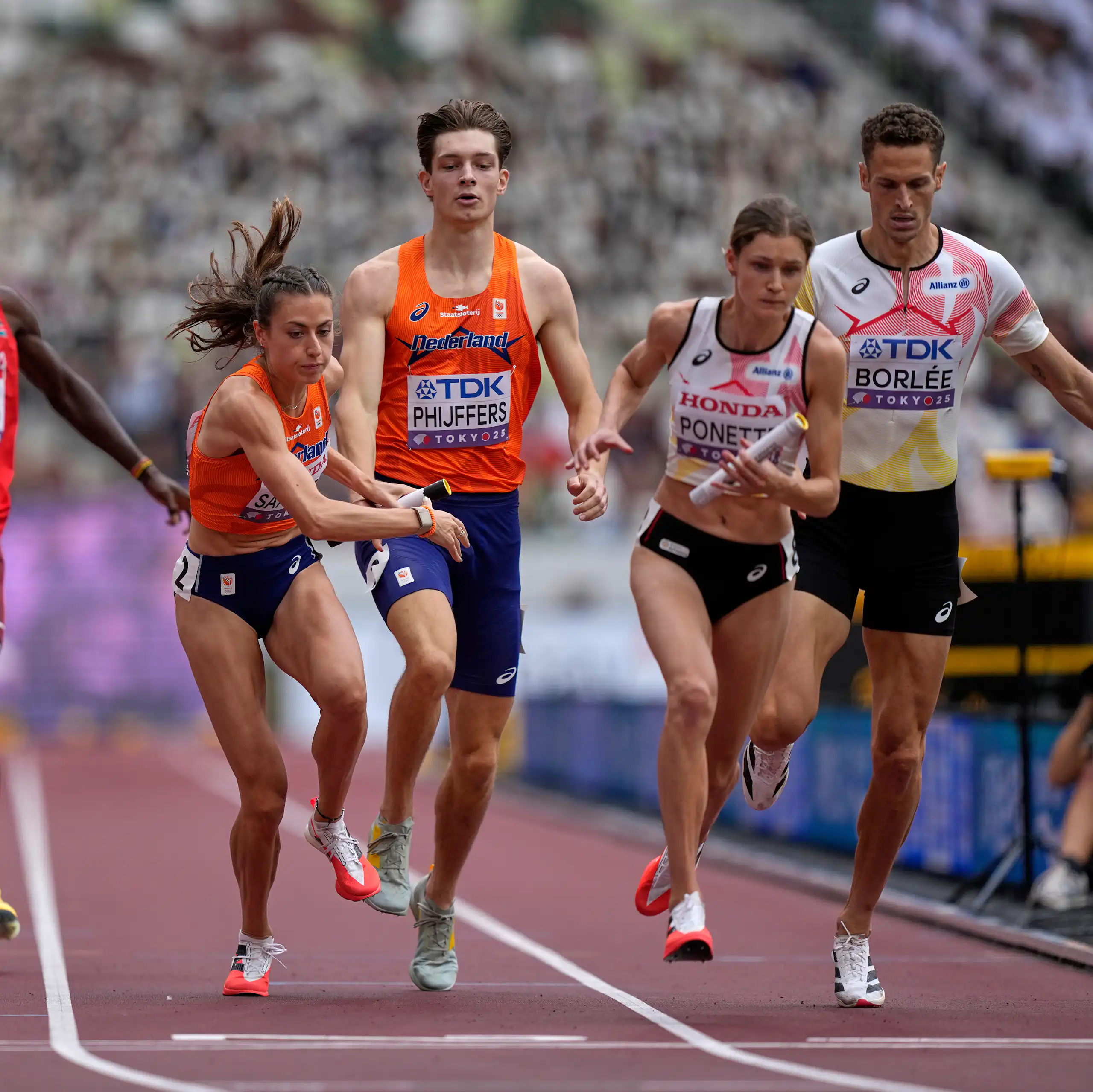 Men and women sprinters handing off batons during a relay race