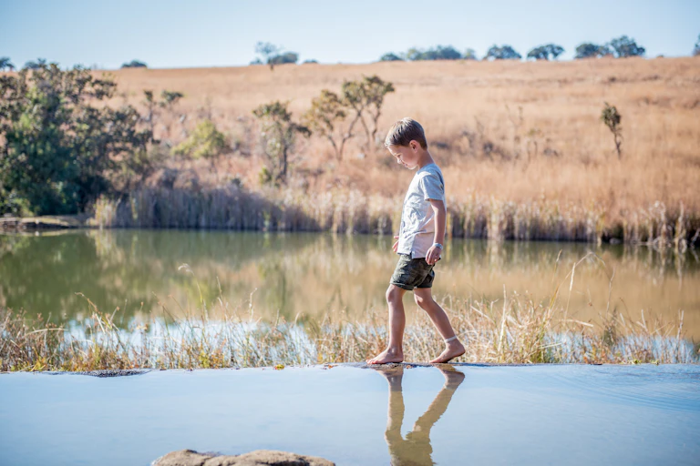 A young boy walks on the edge of a dam on a country property.