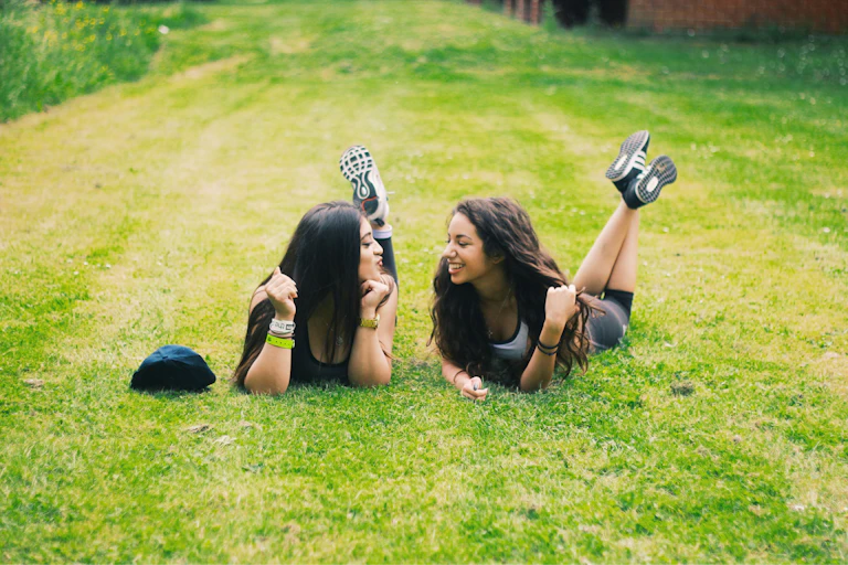 Two teenage girls lying on the grass, laughing with each other.