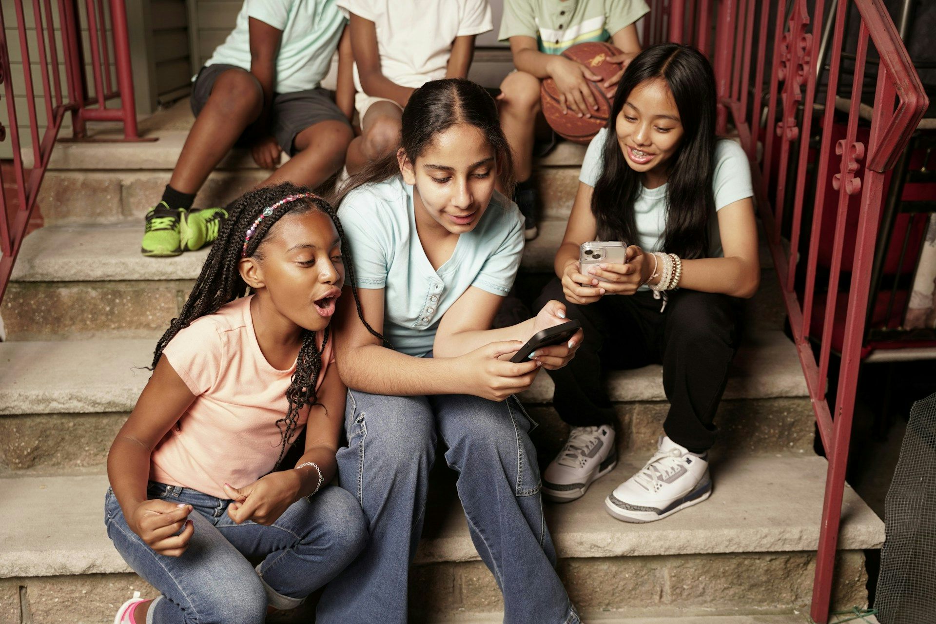 Las adolescentes se sientan juntas en escalones de hormigón, hipnotizadas por los teléfonos inteligentes.