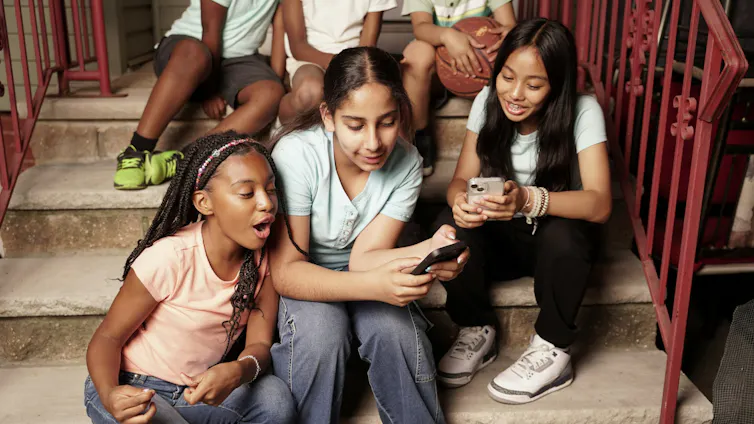 Las adolescentes se sientan juntas en escalones de hormigón, hipnotizadas por los teléfonos inteligentes.