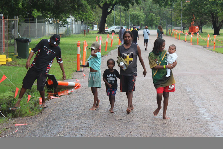 An Indigenous Australian family walks down a previously flooded road.
