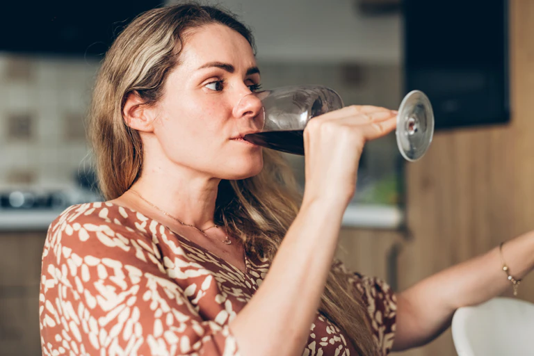 A woman drinks red wine in her kitchen