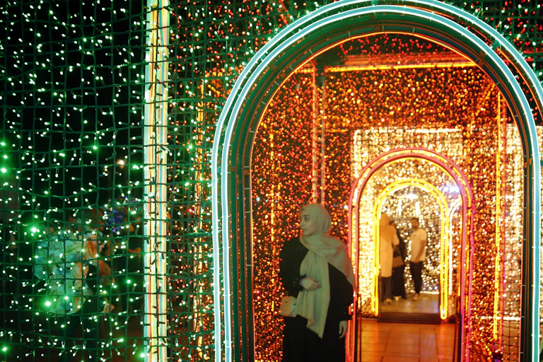 A woman in hijab under a lighted arch at night