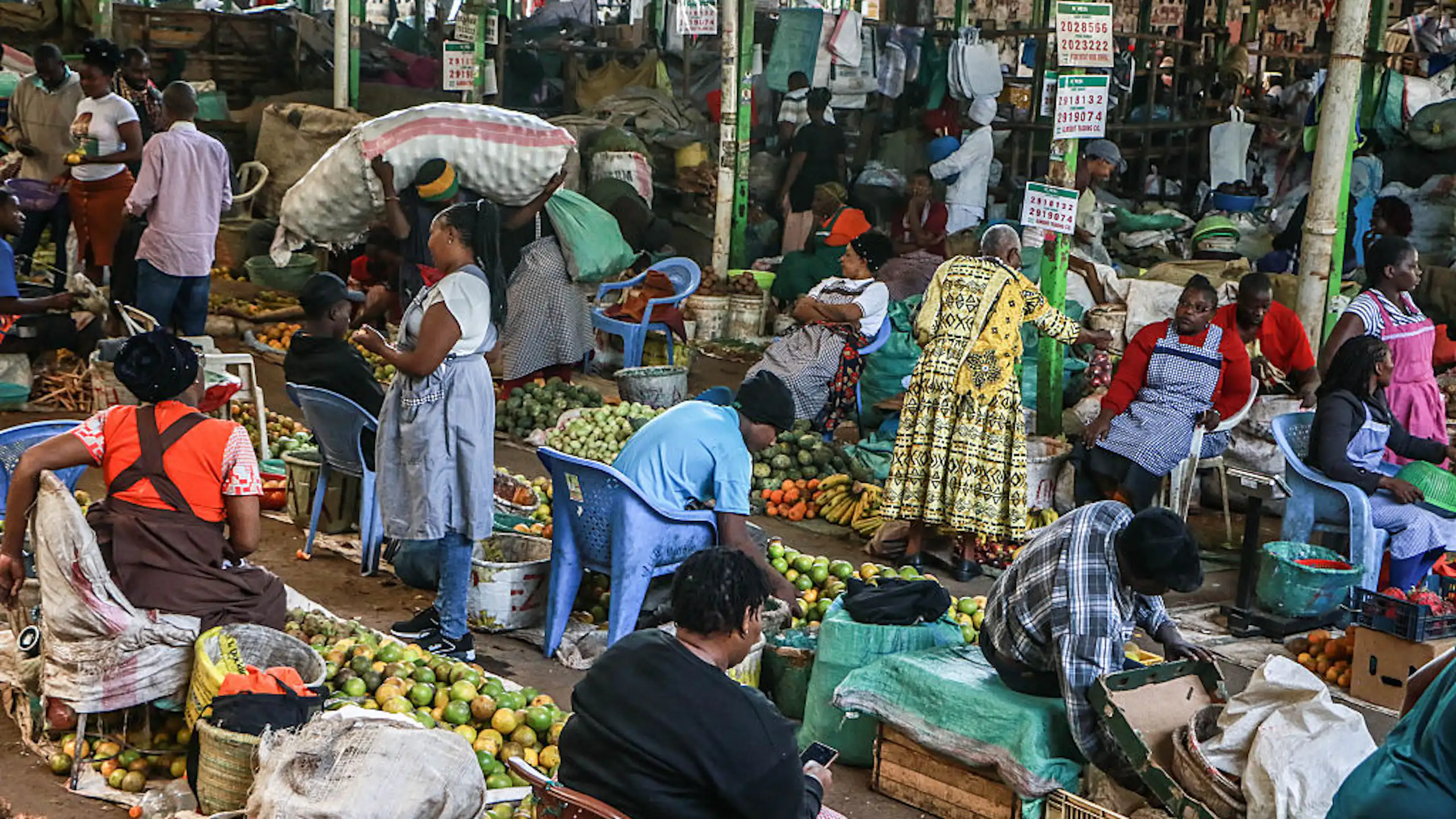 Women seated behind piles of fresh produce on the ground in a marketplace