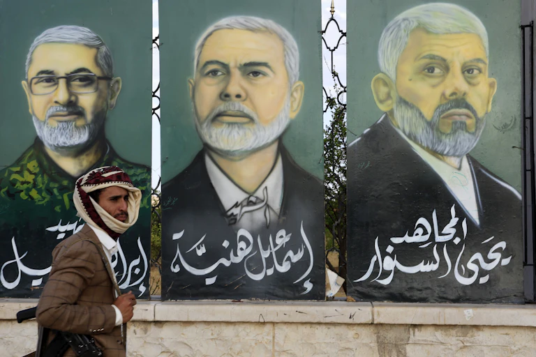 An armed man walks past a mural in Sana'a depicting late military and political figures of Iran-backed proxy groups.