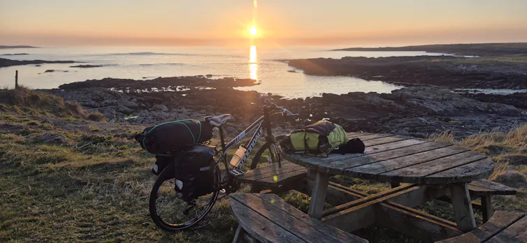 Sun going down over a beach with a bike in the foreground.