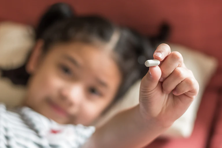 Una mano enseña una pastilla con una cara infantil al fondo