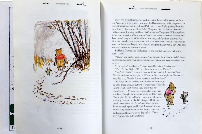 A spread from the children's book Winnie the Pooh with the little bear character walking through a wood with Piglet.