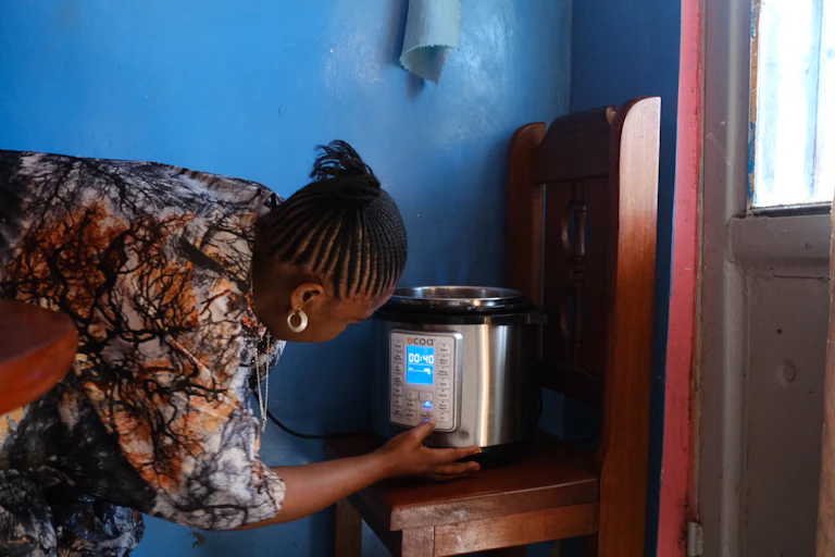 A woman turning on an electric pressure cooker that is standing on a wooden chair with a bright blue wall in the background