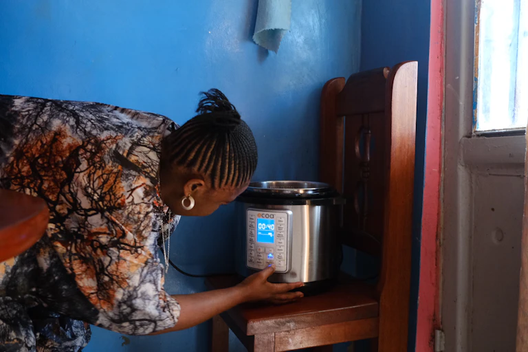 A woman turning on an electric pressure cooker that is standing on a wooden chair with a bright blue wall in the background
