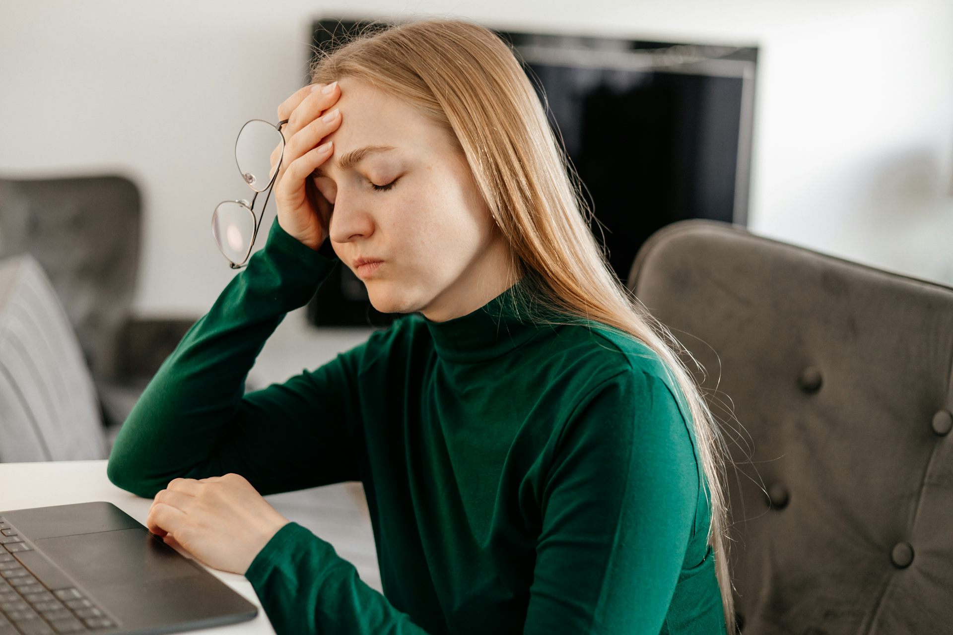 A woman sitting using her laptop holds her head in pain or confusion.