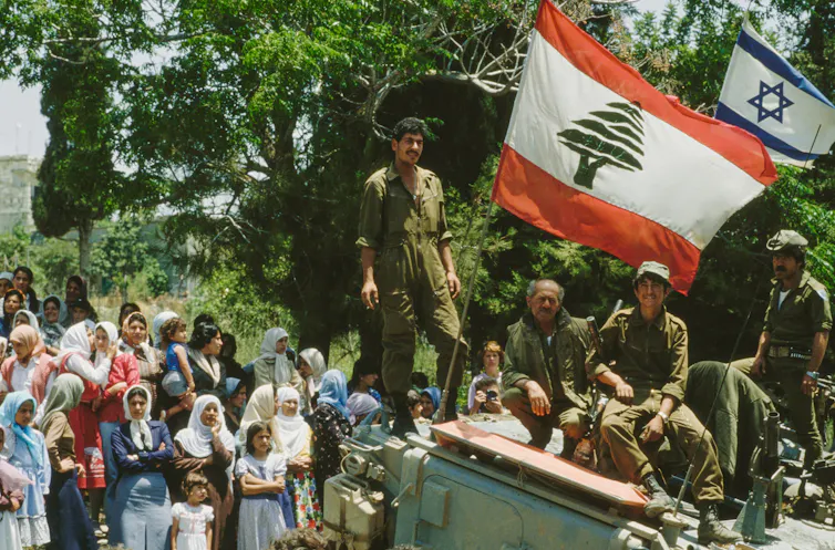 A man stands next to a large flag surrounded by other people