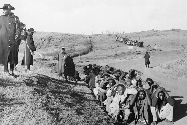 Men huddled on the ground while two others stand towering over them.