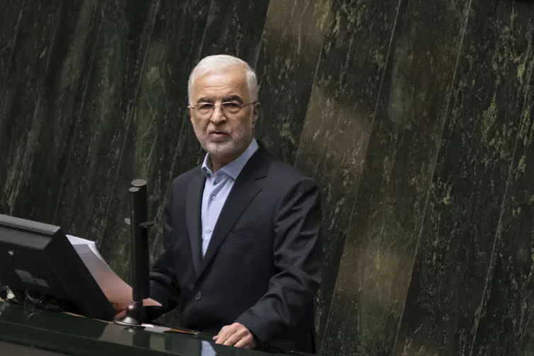 A man in a blazer speaks at a podium.