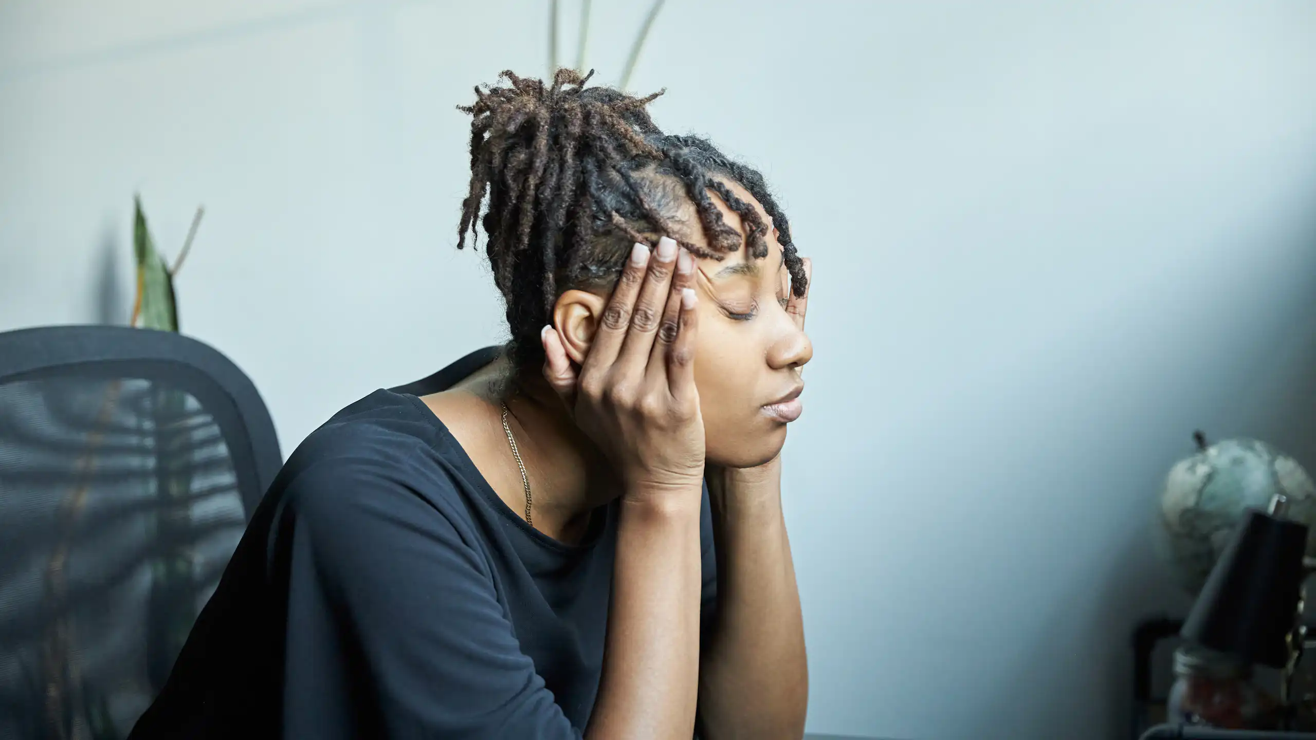 Woman sits at table with eyes closed and fingers on temples