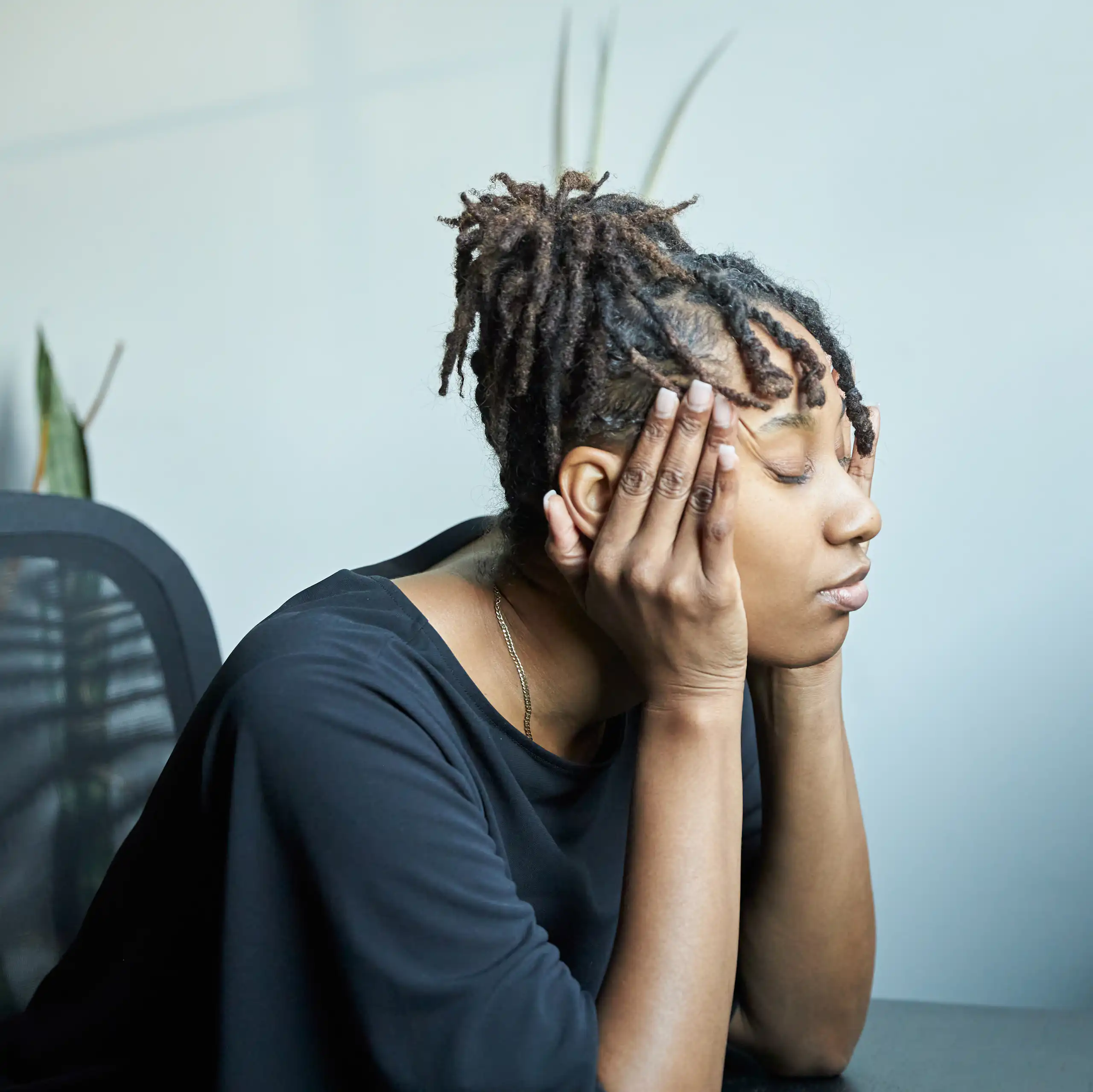 Woman sits at table with eyes closed and fingers on temples