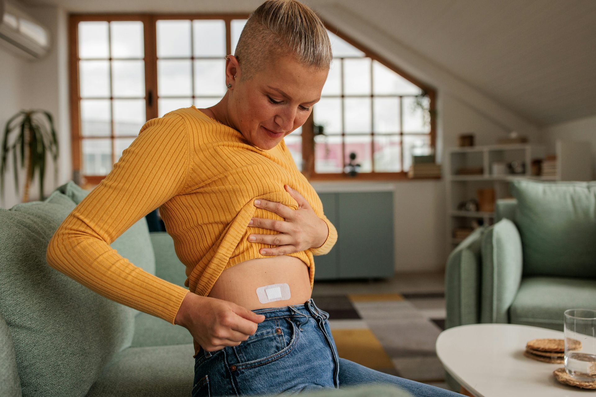 Woman lifts yellow shirt and reveals patch on stomach area
