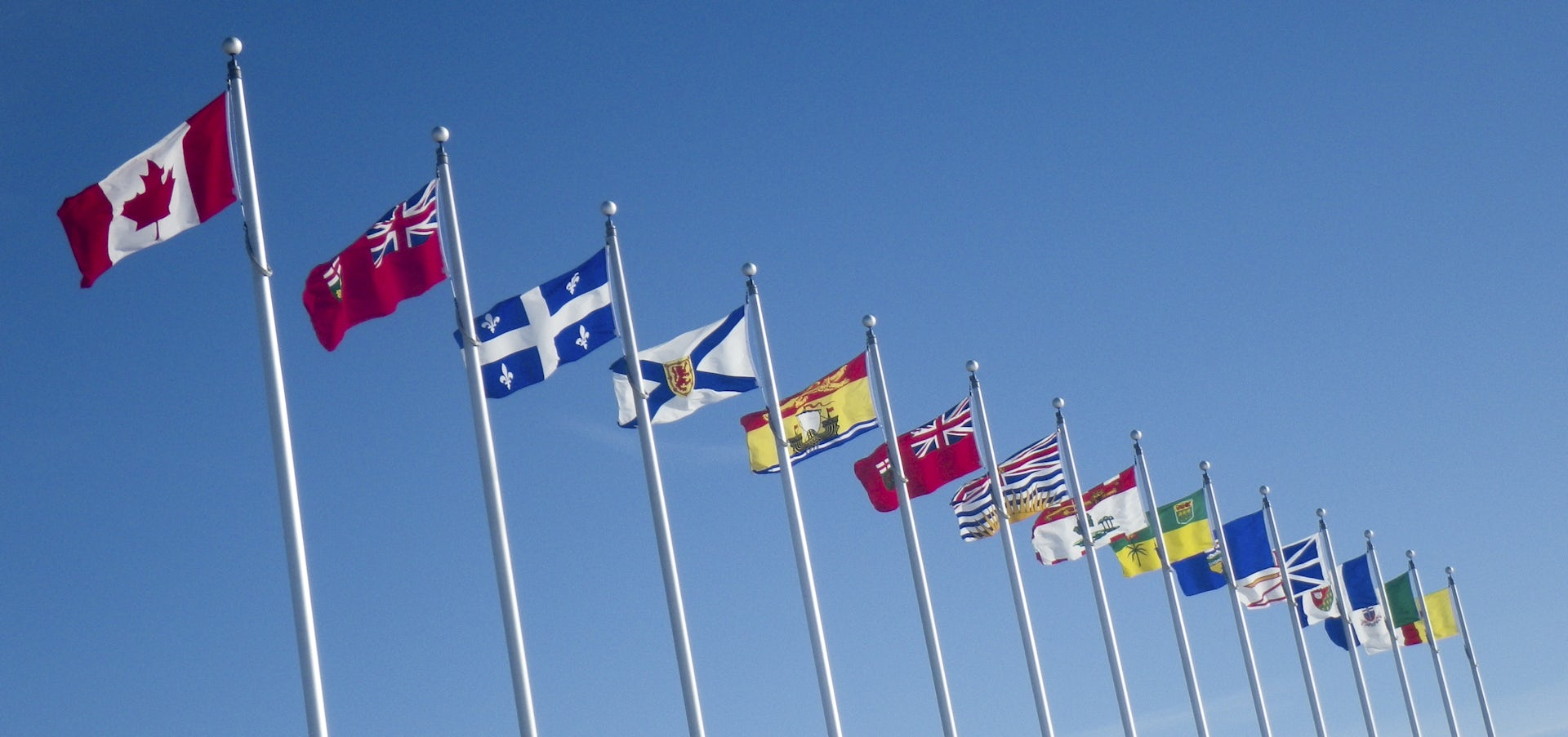 A series of flags shown in a row, leading with a maple leaf Canadian flag followed by flags of provinces.