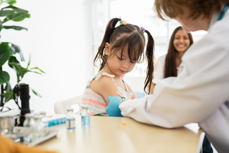 Little girl getting vaccinated at a table with another child behind her.