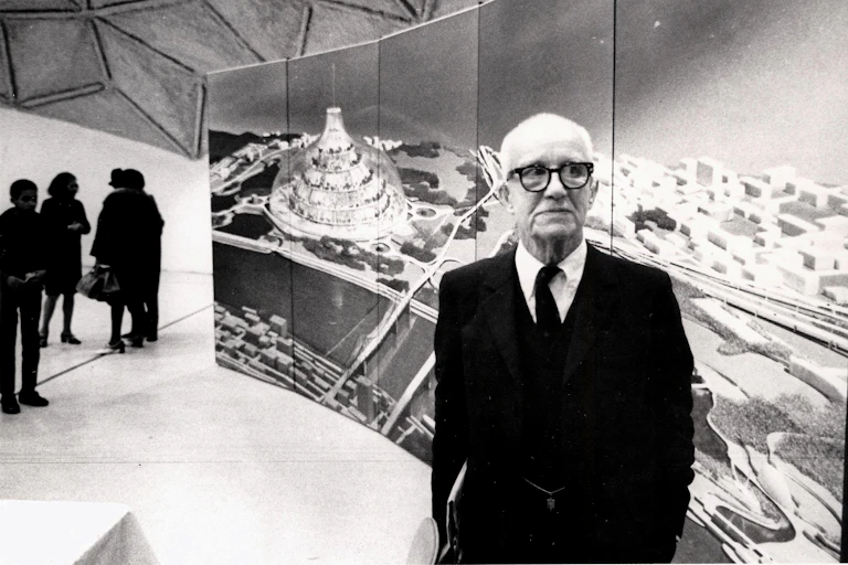 Buckminster Fuller stands in front of a large image of his radical design for a domed city, 1971.