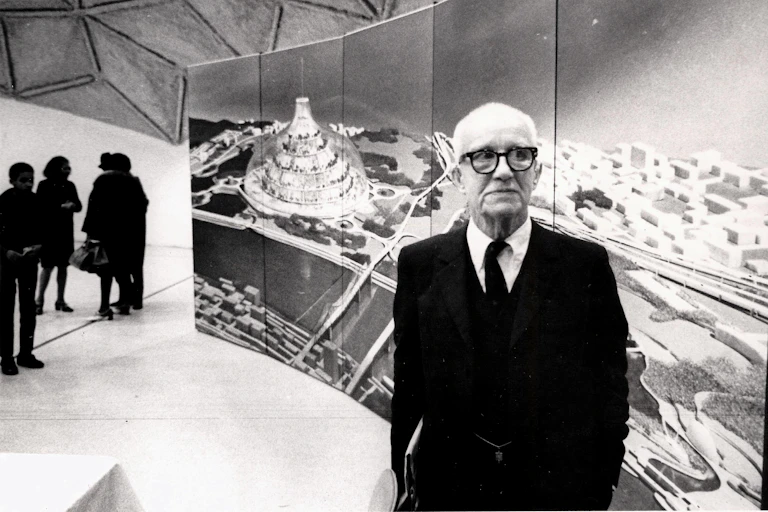 Buckminster Fuller stands in front of a large image of his radical design for a domed city, 1971.