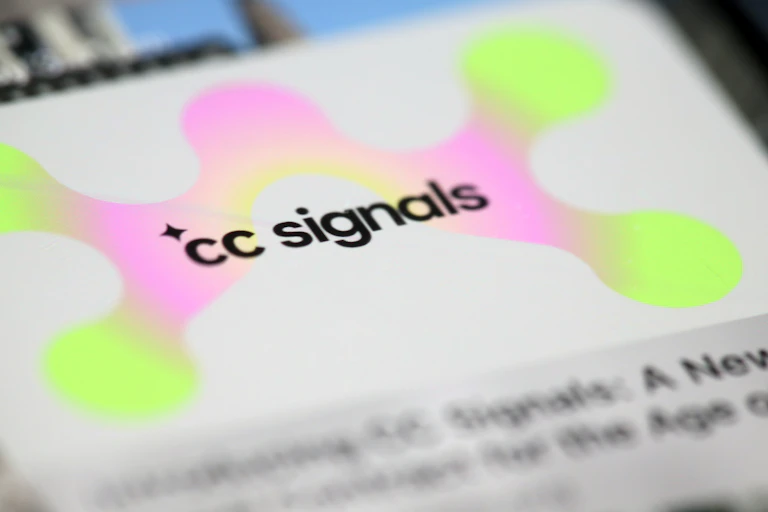 A preview for a webpage with "cc signals" on it next to a sparkle icon and in front of a neon green and pink amorphous shape is seen on a smartphone screen.