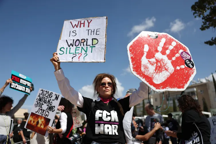 An Israeli protestor holding a placard that says 'Why is the world silent?'
