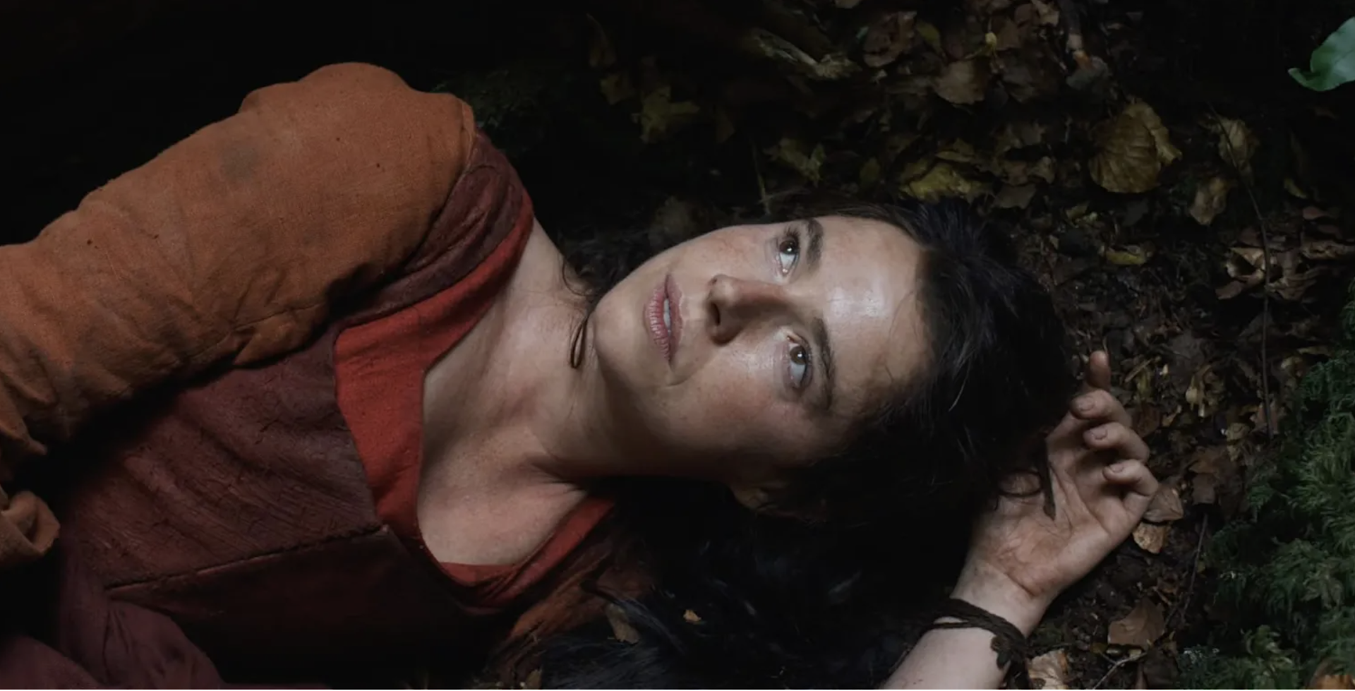 A woman in 16th-century dress lying in the undergrowth looking up at the sky.