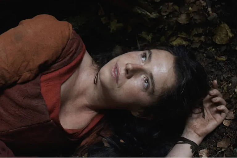 A woman in 16th-century dress lying in the undergrowth looking up at the sky.