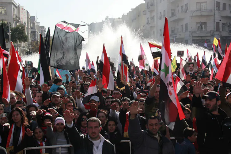 Syrian protestors carrying flags in a large group in 2011.
