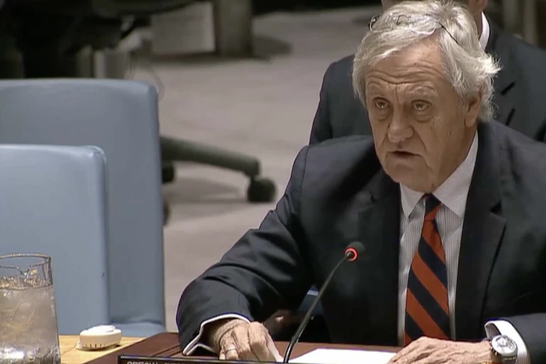 A man in a suit and tie, seated at a microphone