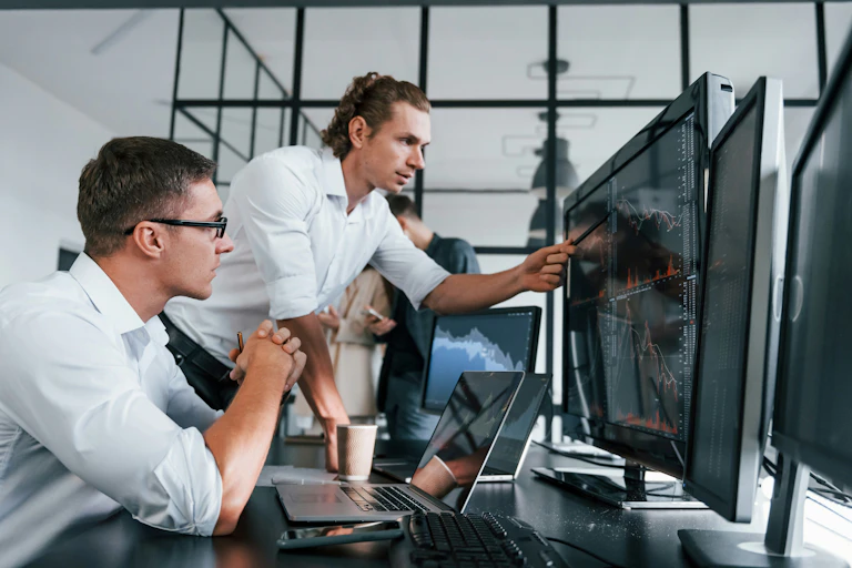 Two white men staring at a computer monitor and discussing what they see.