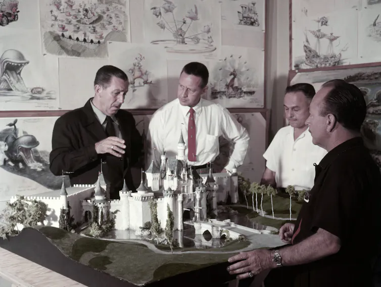 A group of men gathering around a model of a castle and chatting with one another.