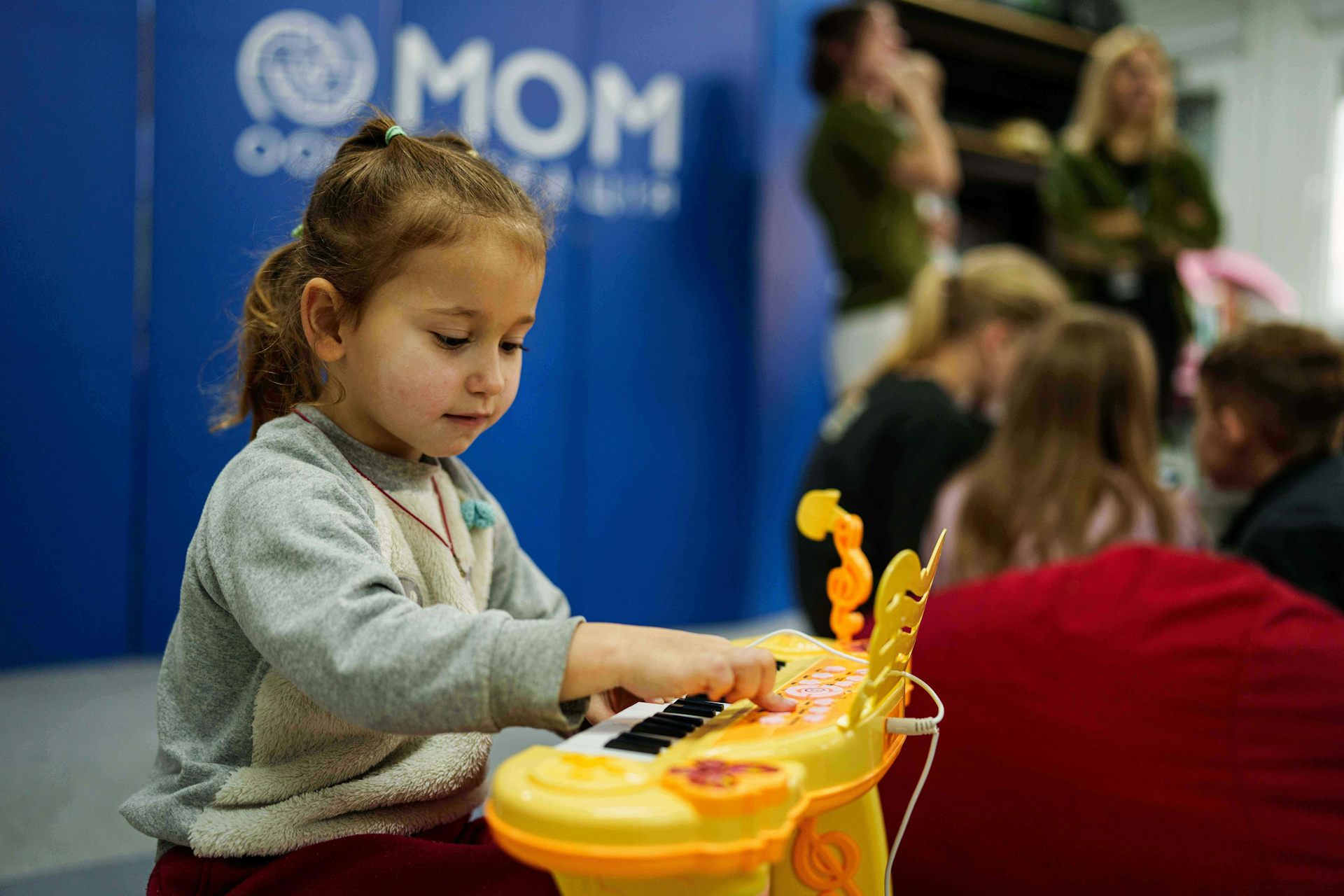 Una joven de cabello oscuro toca con un piano de juguete amarillo.