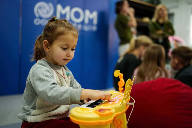 A young dark-haired girl plays with a yellow toy piano.