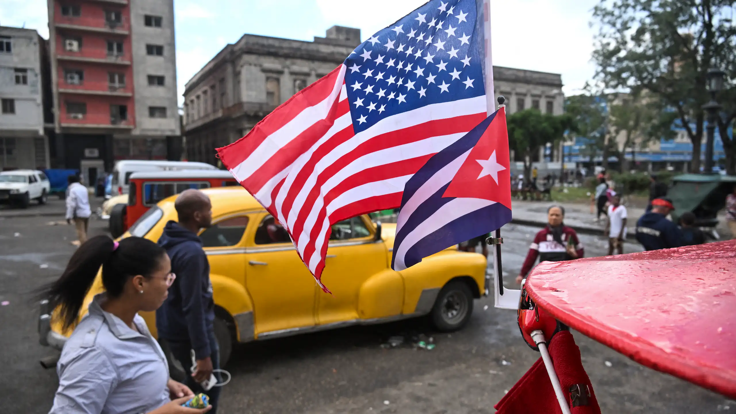 Two flags fly in front of a yellow car.