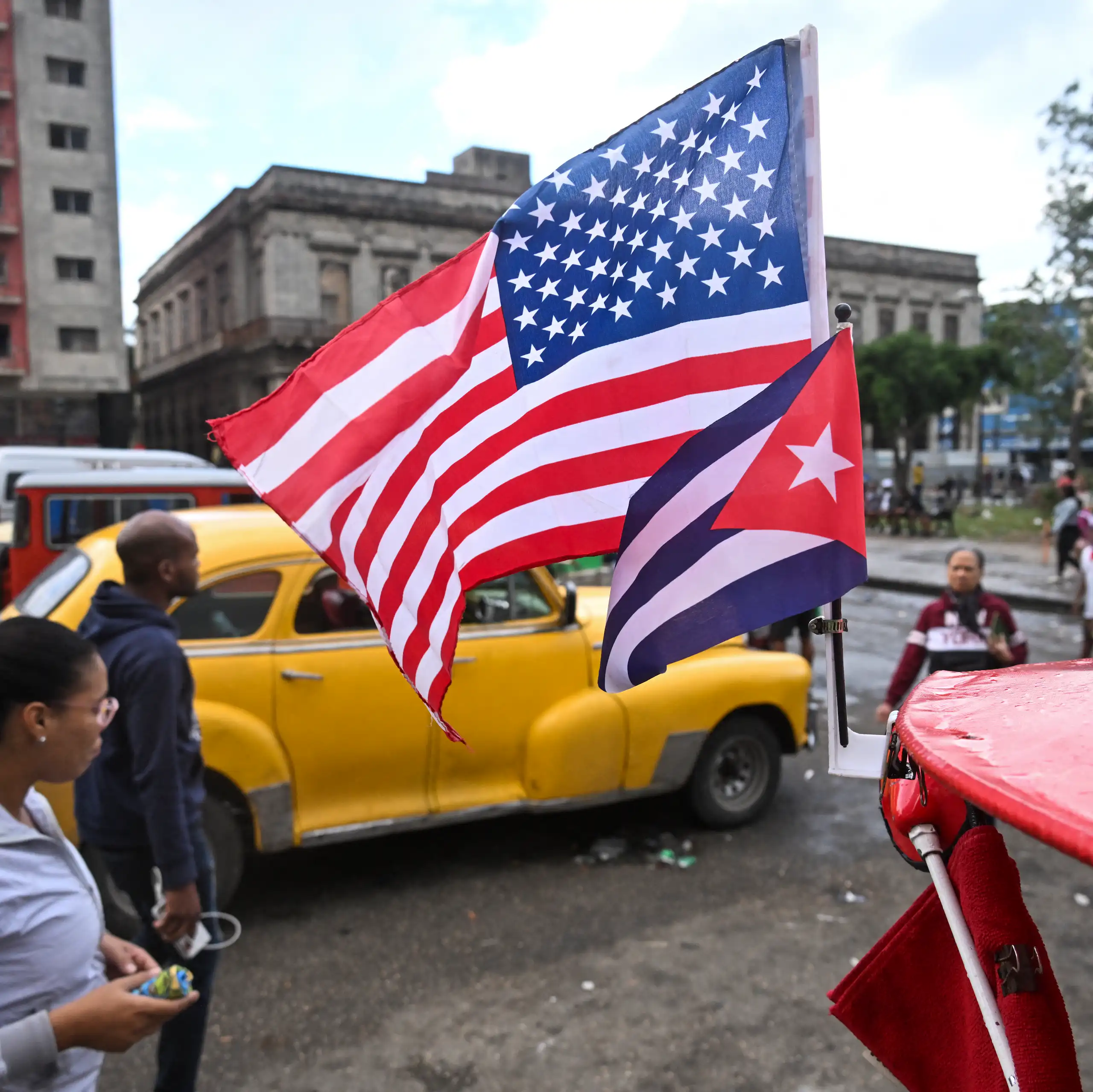 Two flags fly in front of a yellow car.
