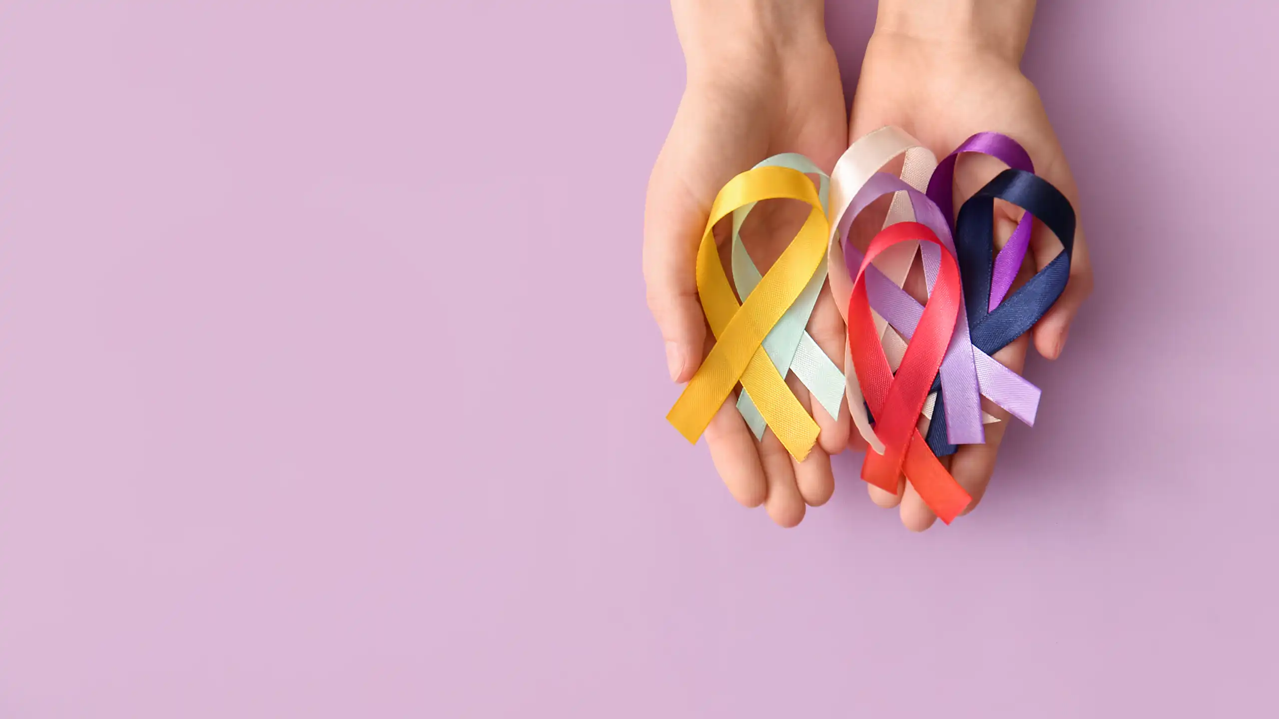 Duas mãos segurando fitas de várias cores que representam diferentes instituições de caridade dedicadas ao combate ao câncer.