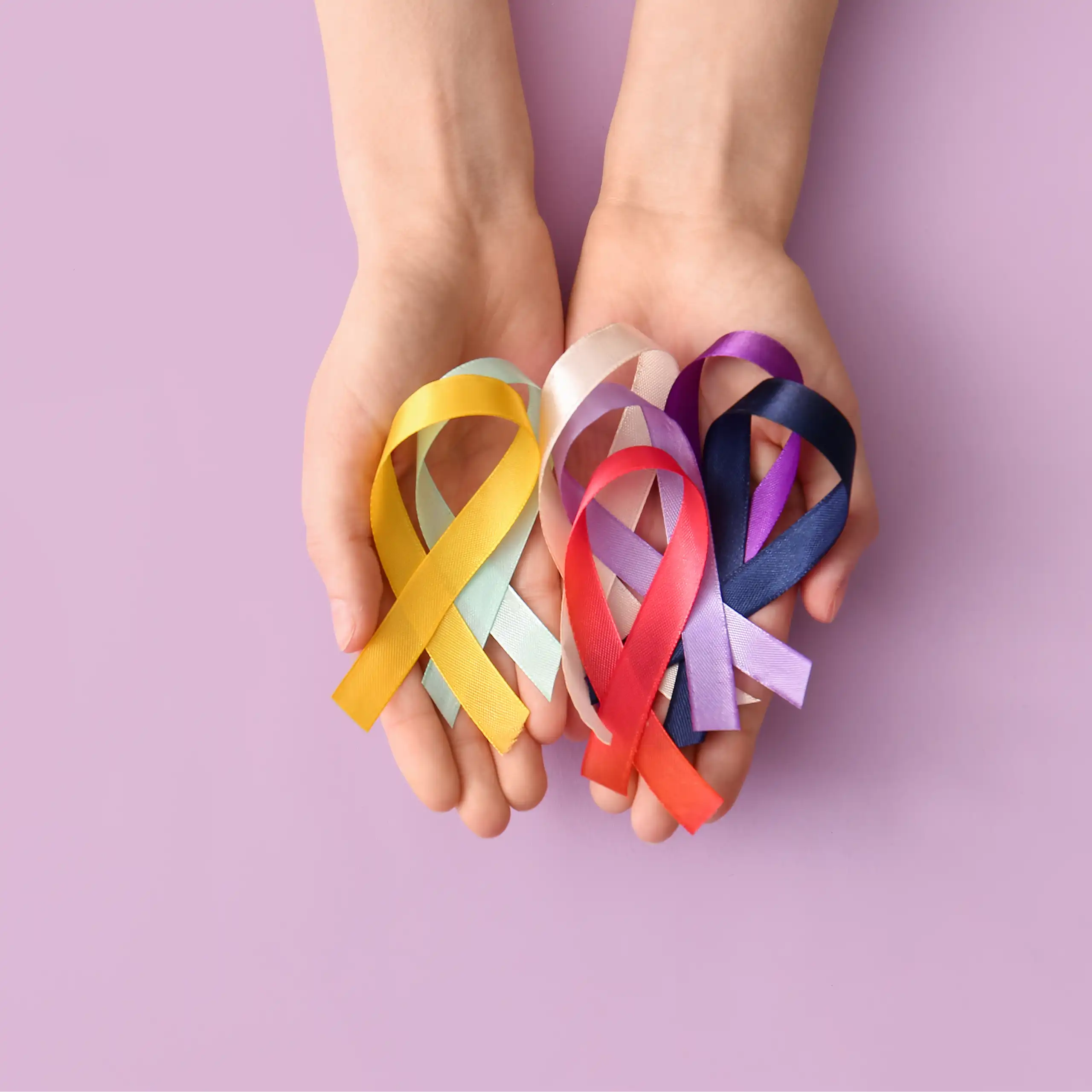 Duas mãos segurando fitas de várias cores que representam diferentes instituições de caridade dedicadas ao combate ao câncer.