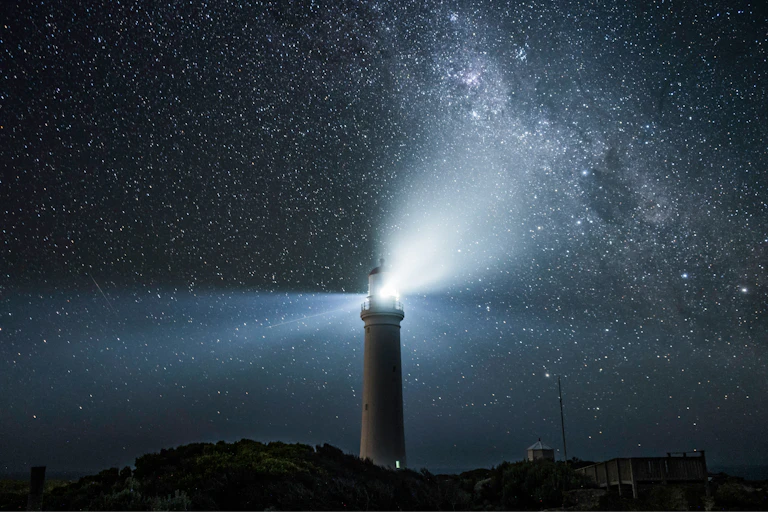 Lighthouse shines under a starry sky.