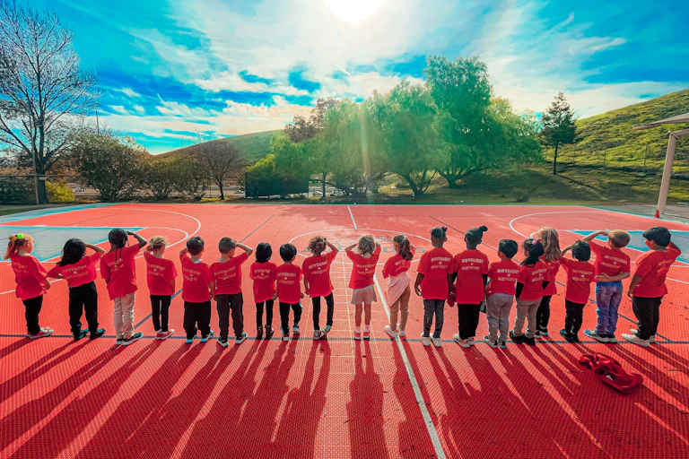 A group of children line up on an outdoor sport court.